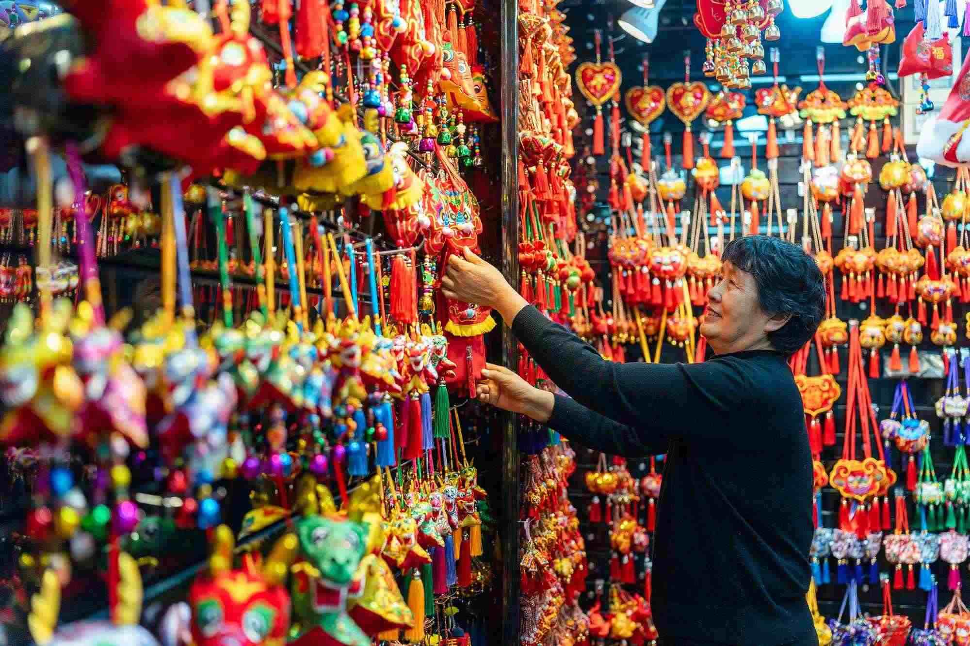 2023年12月11日，金華義烏國際商貿(mào)城，龍年喜慶用品掛滿攤位，顧客正在挑選中。