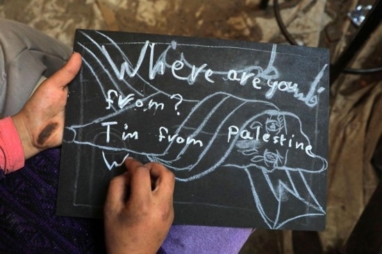 2023年12月28日，一名學(xué)生在加沙地帶南部城市拉法一所學(xué)校的臨時教室中寫下“我來自巴勒斯坦”的字樣。新華社發(fā)（里澤克·阿卜杜勒賈瓦德攝）