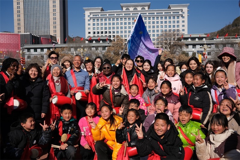 中外青年學子在安塞文化廣場觀看陜北腰鼓和大秧歌表演后合影留念，大家踏著鼓點共舞，翻飛的紅綢與躍動的身影交織，在黃土地廣場上繪出一幅生動的陜北民俗互動畫卷